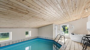 En inomhuspool med träbjälkar i taket, ett kaklat golv och utsikt över utomhusmiljön genom en dörr.