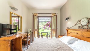 Una camera da letto con un letto, una scrivania con televisore, una sedia, un tavolo con due sedie e vista su un giardino attraverso una porta aperta.