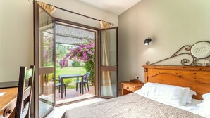Una camera da letto con un letto, un comodino in legno, una scrivania e una sedia. C'è una porta scorrevole in vetro che dà su uno spazio esterno con un tavolo e sedie.