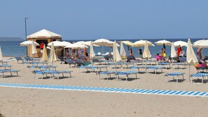 Una spiaggia con file di lettini e ombrelloni, una torretta di salvataggio e il mare sullo sfondo.
