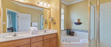 A bathroom with a double vanity, a bathtub, a shower, and a large mirror with lights.