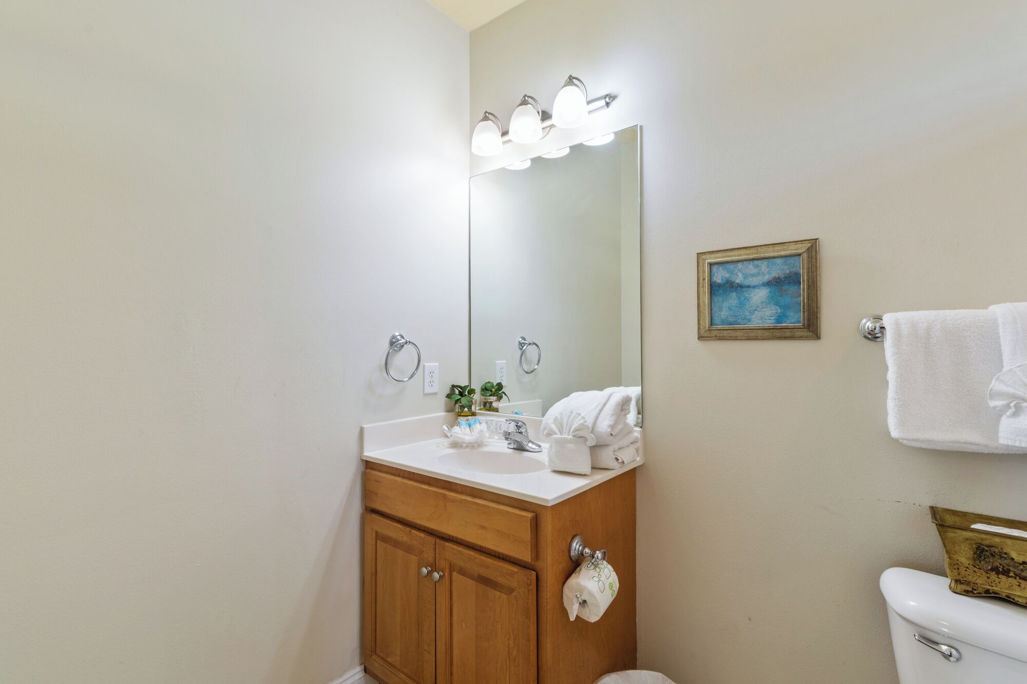 Un baño con tocador de madera, un lavamanos, un espejo con luces, un inodoro y un perchero para toallas.