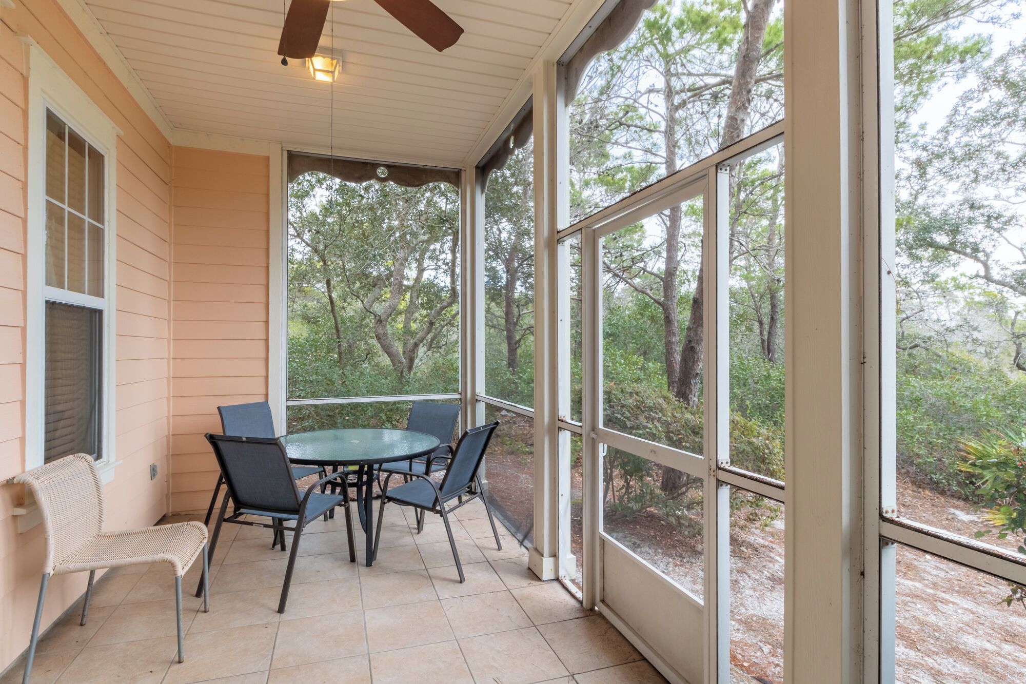 Une terrasse couverte avec une table et des chaises, de grandes fenêtres et un ventilateur de plafond.