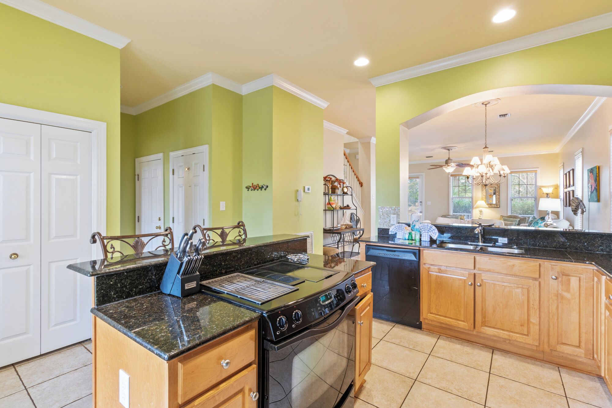 A kitchen with a central island, wooden cabinets, a stove, and a dining area with a chandelier.