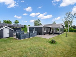 Ein modernes Mobilheim mit Terrasse, einem kleinen Geräteschuppen und einem umzäunten Garten.
