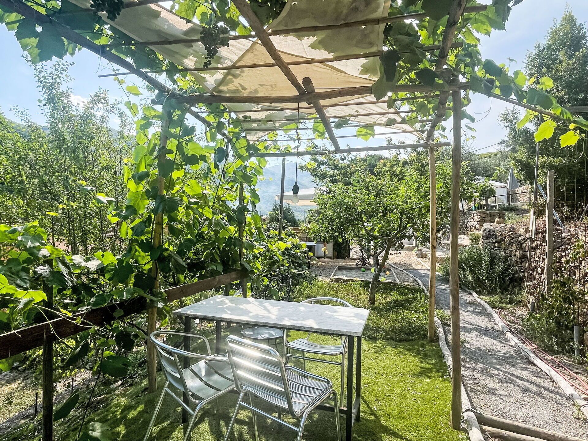 Een overdekt terras met een tafel en stoelen, omringd door groen en uitzicht op het landschap.