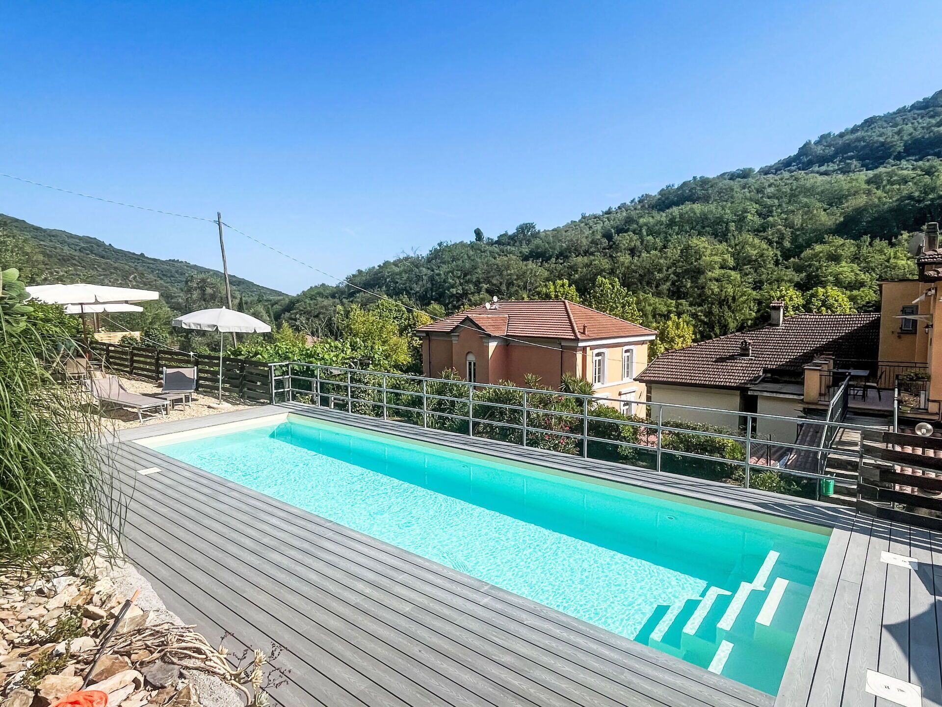 Une piscine entourée de maisons et de verdure, avec une terrasse en bois.