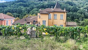A yellow building with a red roof, surrounded by greenery and a hill in the background. - Cosy apartment for 4 people with WIFI, pool, TV, patio and pets allowed (Dolcedo)