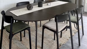A dining area with a round table, black chairs, a white brick wall, and framed artwork.