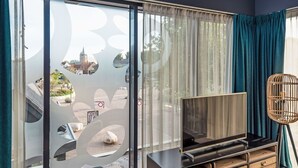 Ein Zimmer mit einer großen Schiebeglaswand, einem Fernseher auf einer Holzkommode und einer Weidenflechtlampe.