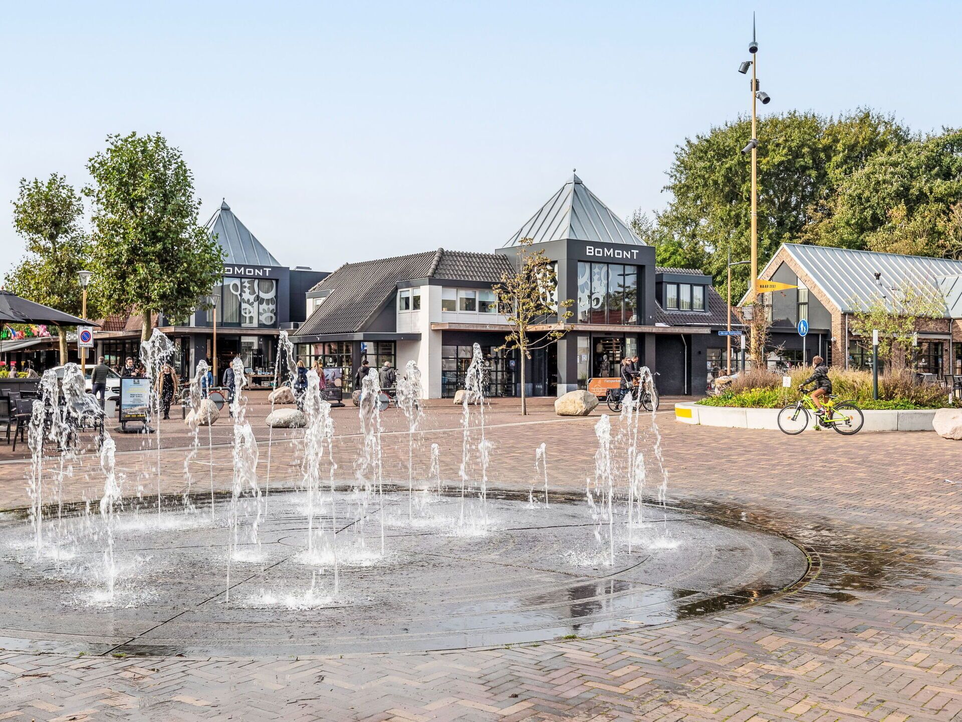 Une place publique dotée d’une fontaine centrale, entourée de bâtiments abritant des commerces.