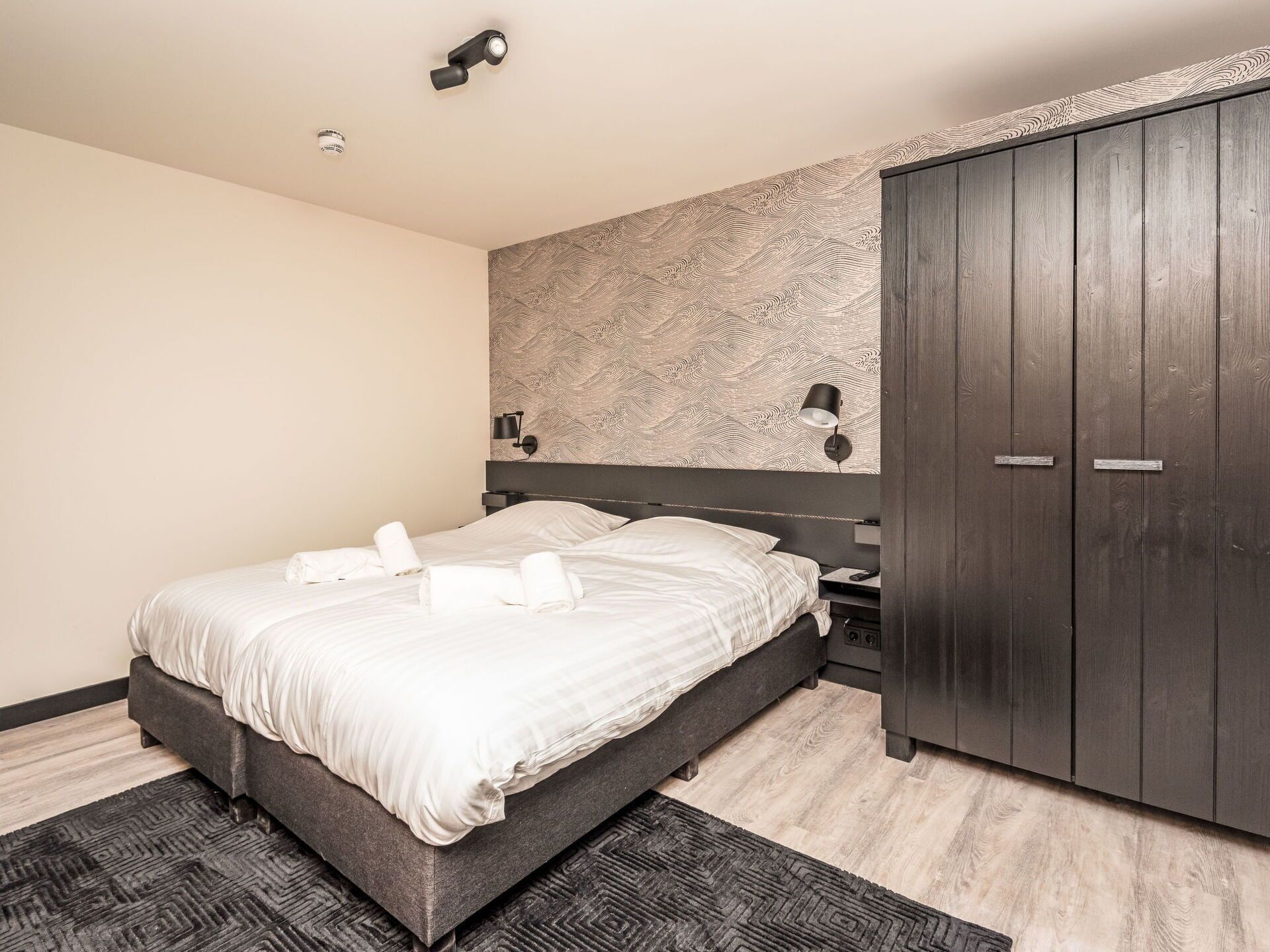 Een moderne slaapkamer met een bed, een garderobe en een behang met patroon.