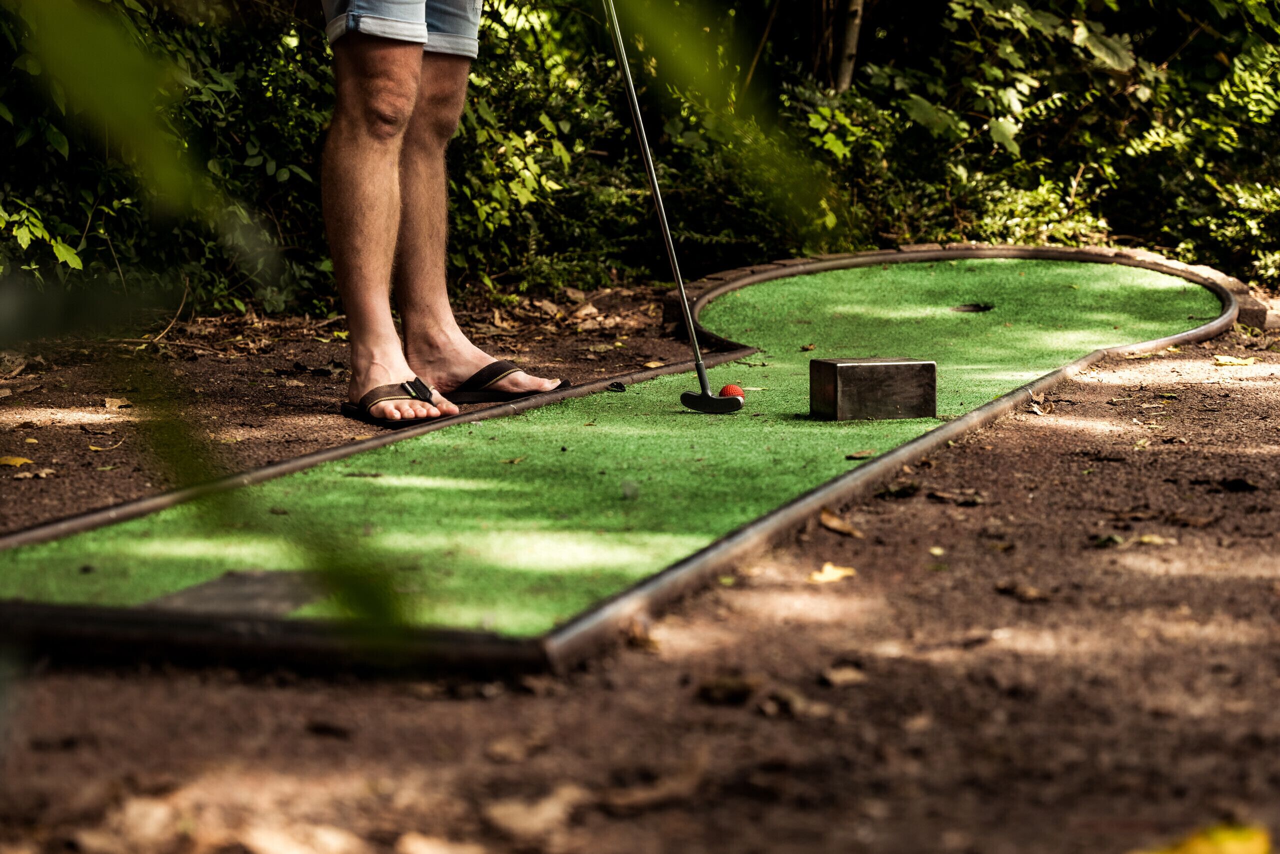 A person playing mini-golf with a putter and ball on a green artificial turf.