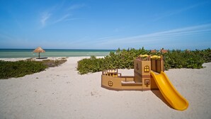 Une plage avec une aire de jeux, comprenant un toboggan et un parasol en chaume.
