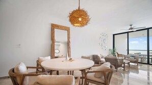 Un salon moderne avec une table à manger ronde, des meubles en osier, un grand miroir et une vue sur l’extérieur.