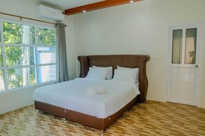 Relax in a spacious room with a large bed, wooden floor, and a window offering a view of lush greenery.