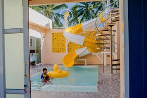 A pool area with a water slide and a child playing in the water.
