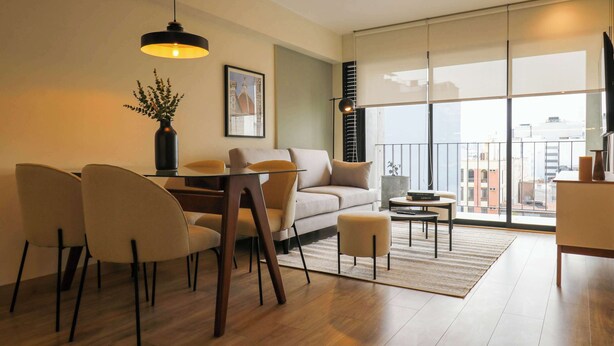 Una sala de estar moderna con un sofá, mesa de comedor, sillas, una mesita de centro y un ventanal con vistas a la ciudad.