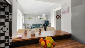 Een moderne woonkamer met een houten eettafel, een schaal met fruit en een bordje met de tekst 'Water besparen'.