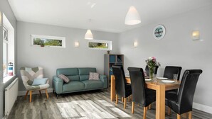 Een moderne woonkamer met een groene bank, een houten eettafel, zwarte stoelen en een visgraatvloer.