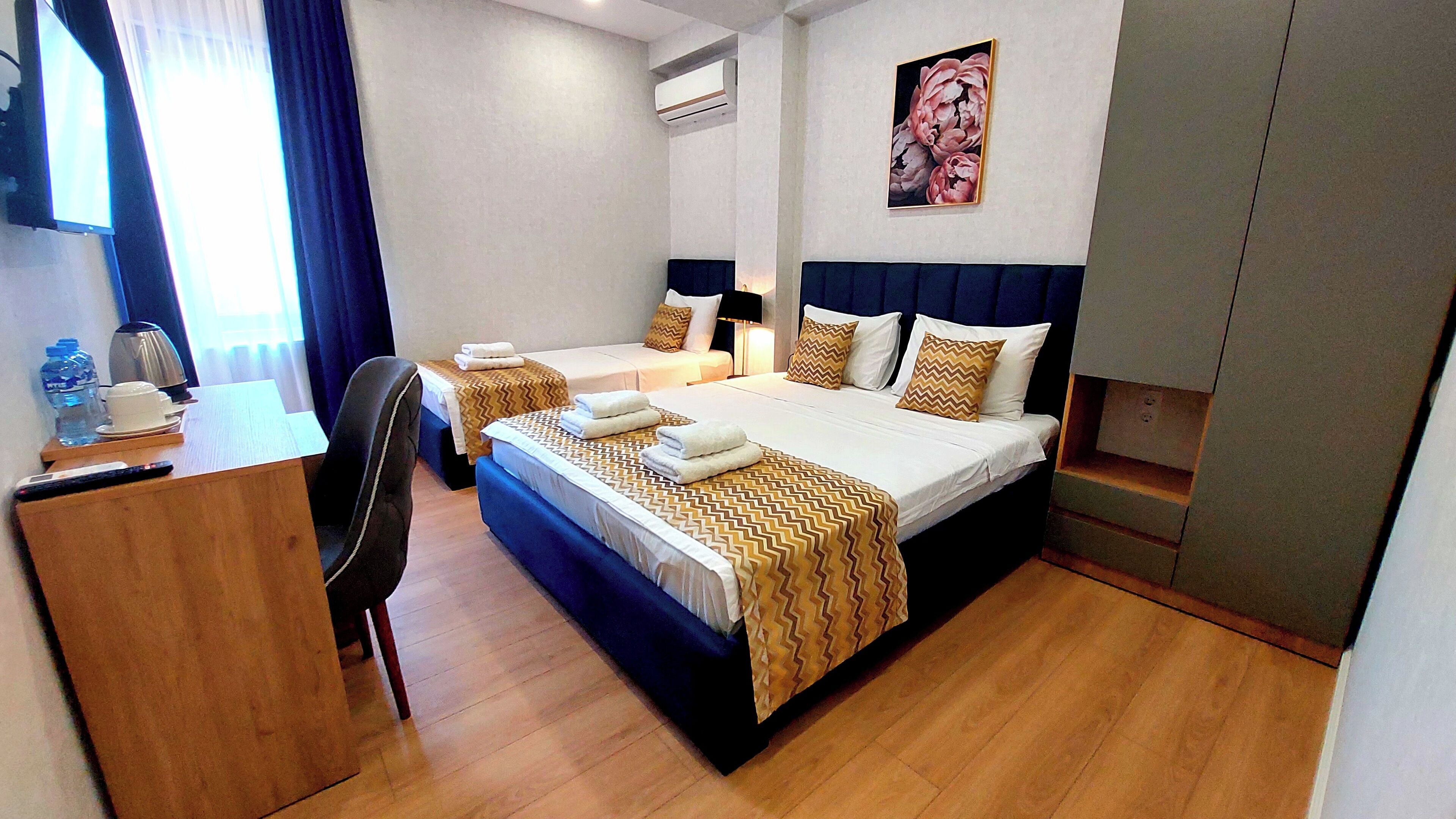 A hotel room with two beds, a desk, a chair, a coffee maker, and a painting on the wall.