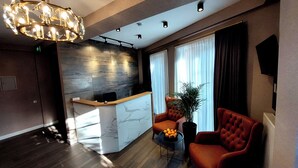 A modern reception area with a marble counter, a large chandelier, and two plush armchairs. - Falcon Boutique Hotel (Tbilisi)
