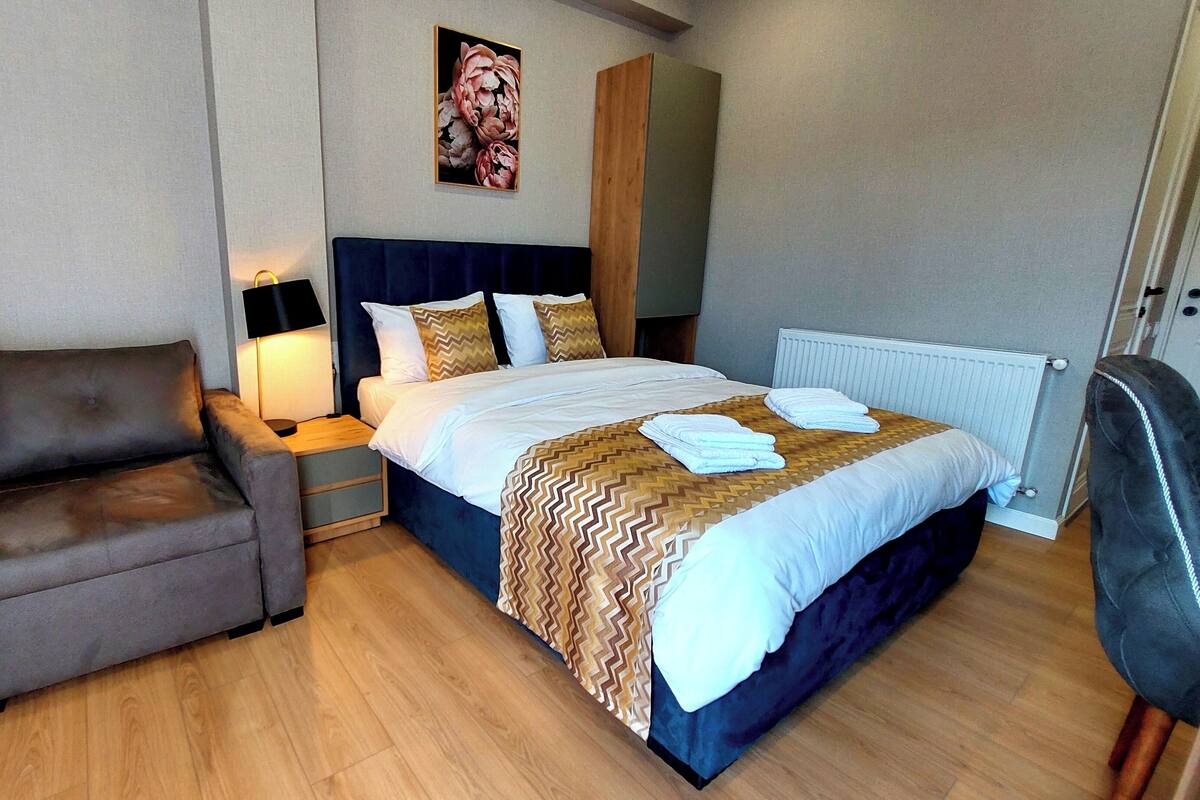 Una habitación de hotel con cama, una silla, una mesita de noche, una lámpara y un radiador.