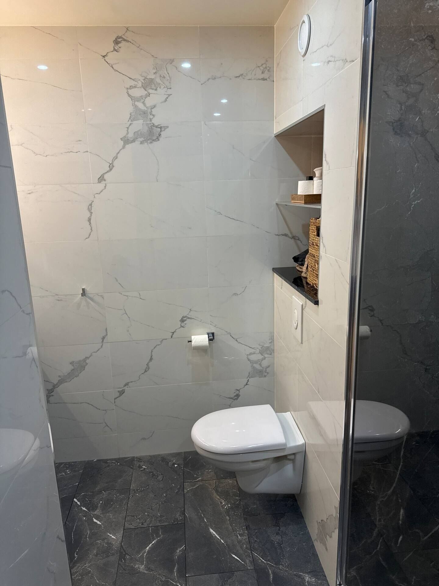 Une salle de bain moderne avec des toilettes, un espace douche et des carreaux de marbre.