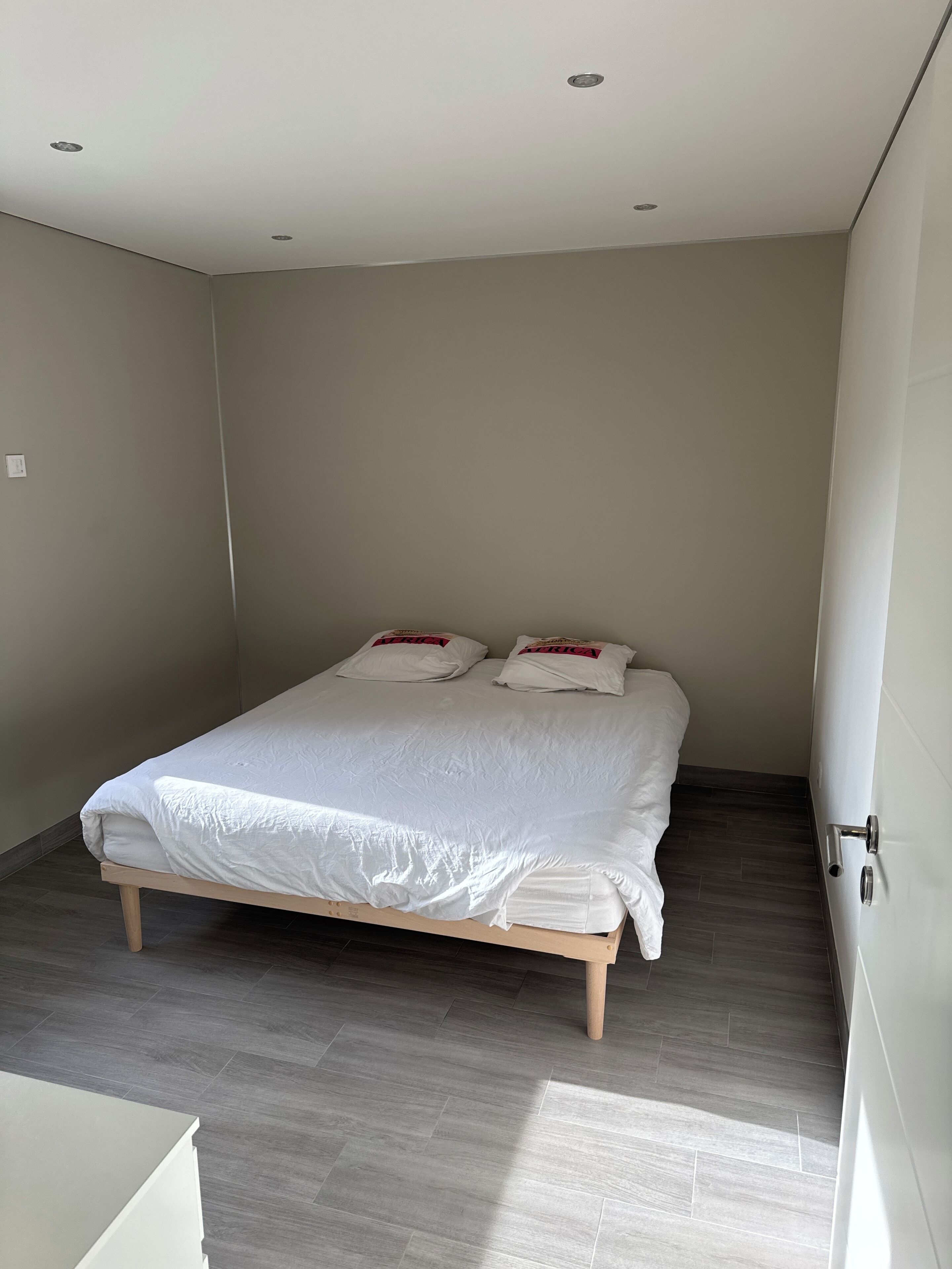 Un dormitorio con cama, piso de madera y pared blanca.
