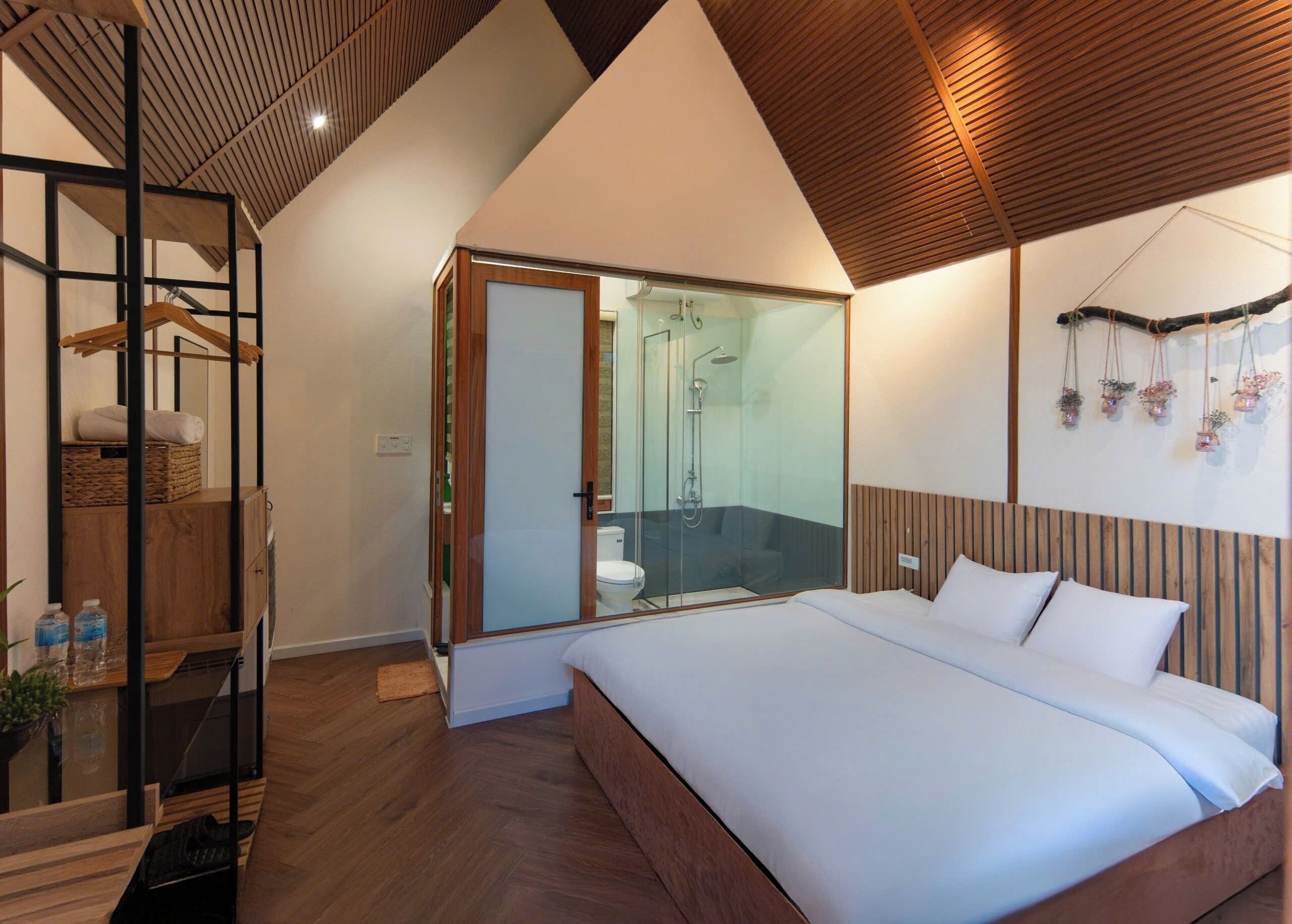 Un dormitorio con una cama grande, cabecero de madera, mampara de cristal para la ducha y techo de madera.