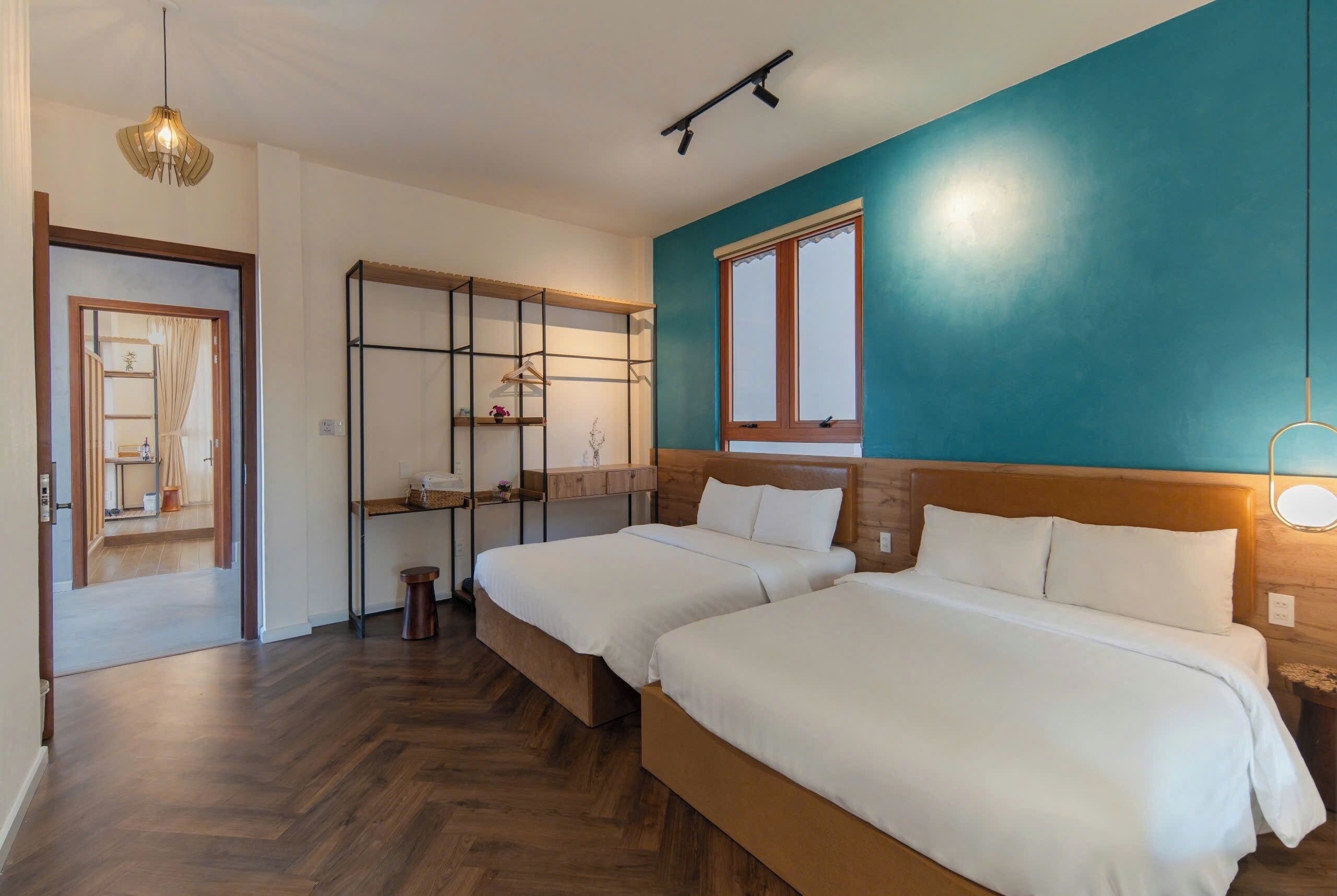 Une chambre d’hôtel avec deux lits, une tête de lit en bois, une fenêtre et un luminaire suspendu.
