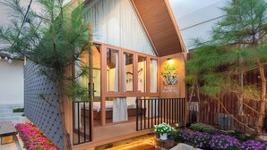 A bungalow with a wooden exterior, a balcony with a railing, and a garden with various plants and flowers. - Mê Villa Dalat (Xuan Huong - Da Lat)