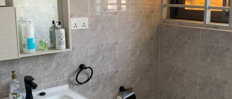 A bathroom with a white sink, mirror, and toilet. There is a window with bars, a towel rack, and a toilet paper holder.
