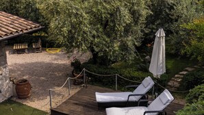 Un espace piscine aménagé avec des chaises longues et un parasol, entouré de verdure et offrant une vue sur un plan d’eau.