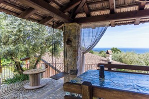 A wooden table and bench under a covered patio with a stone pillar and a view of the sea. - Positano Villa with View - Large Garden and Private Pool - 3 bedrooms 2 bathrooms (Lazio)