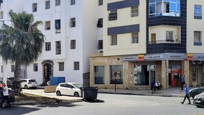 Un immeuble à plusieurs étages doté de balcons, une banque et des voitures garées.