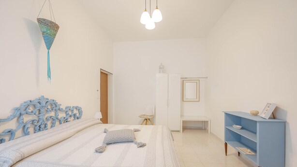 Een slaapkamer met een bed, een blauw hoofdbord, een witte kledingkast, een blauwe nachtkastje en een hangende lamp.