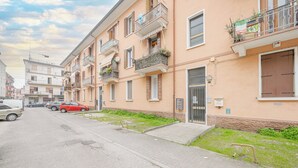Een appartementencomplex met meerdere balkons, een hekwerk en een parkeerplaats met auto's.