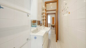 Een smalle badkamer met witte tegels, een wastafel en een spiegel.