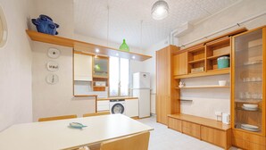 Een kleine keuken met een eettafel, houten keukenkastjes, een wasmachine en een koelkast.