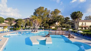 En stor udendørs swimmingpool med flere baner, omgivet af liggestole og palmer.