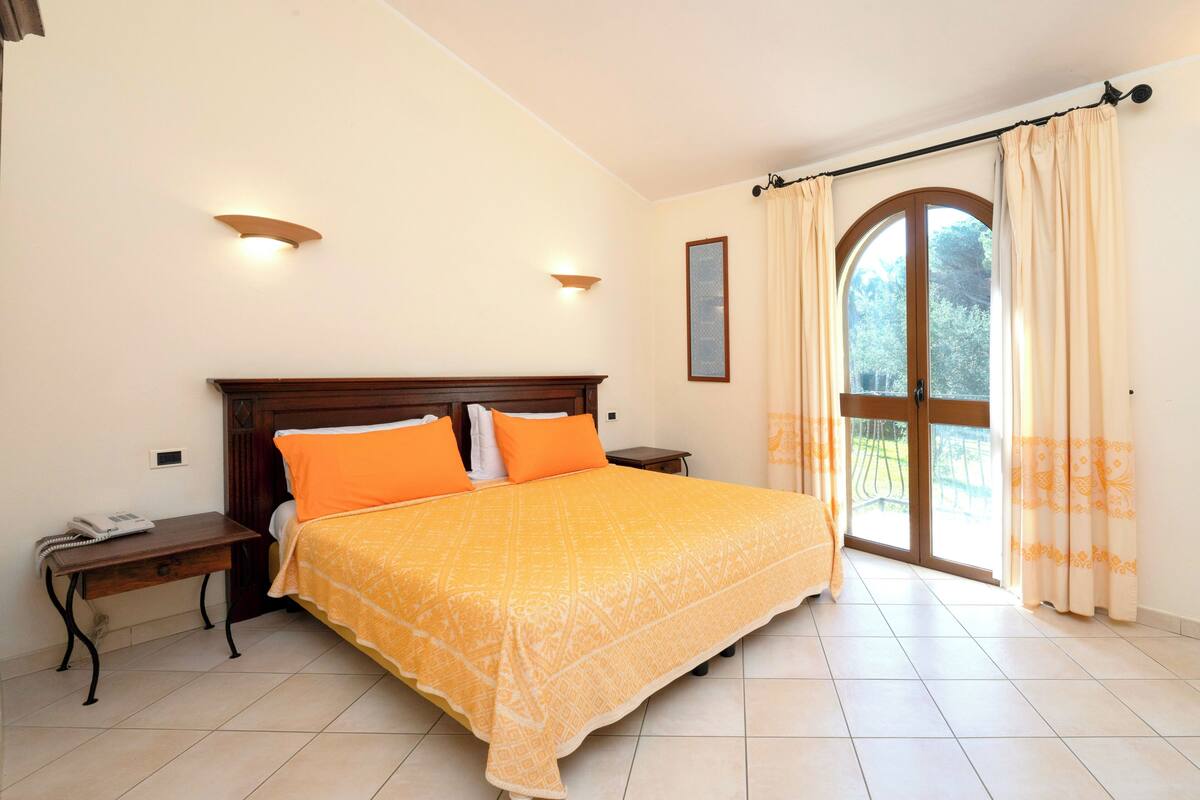 Une chambre à coucher avec un grand lit, deux tables de chevet, une commode et une fenêtre avec des rideaux.