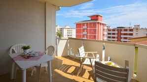 Un balcon avec une table et des chaises, un pot de fleurs et une vue sur des bâtiments rouges en arrière-plan.