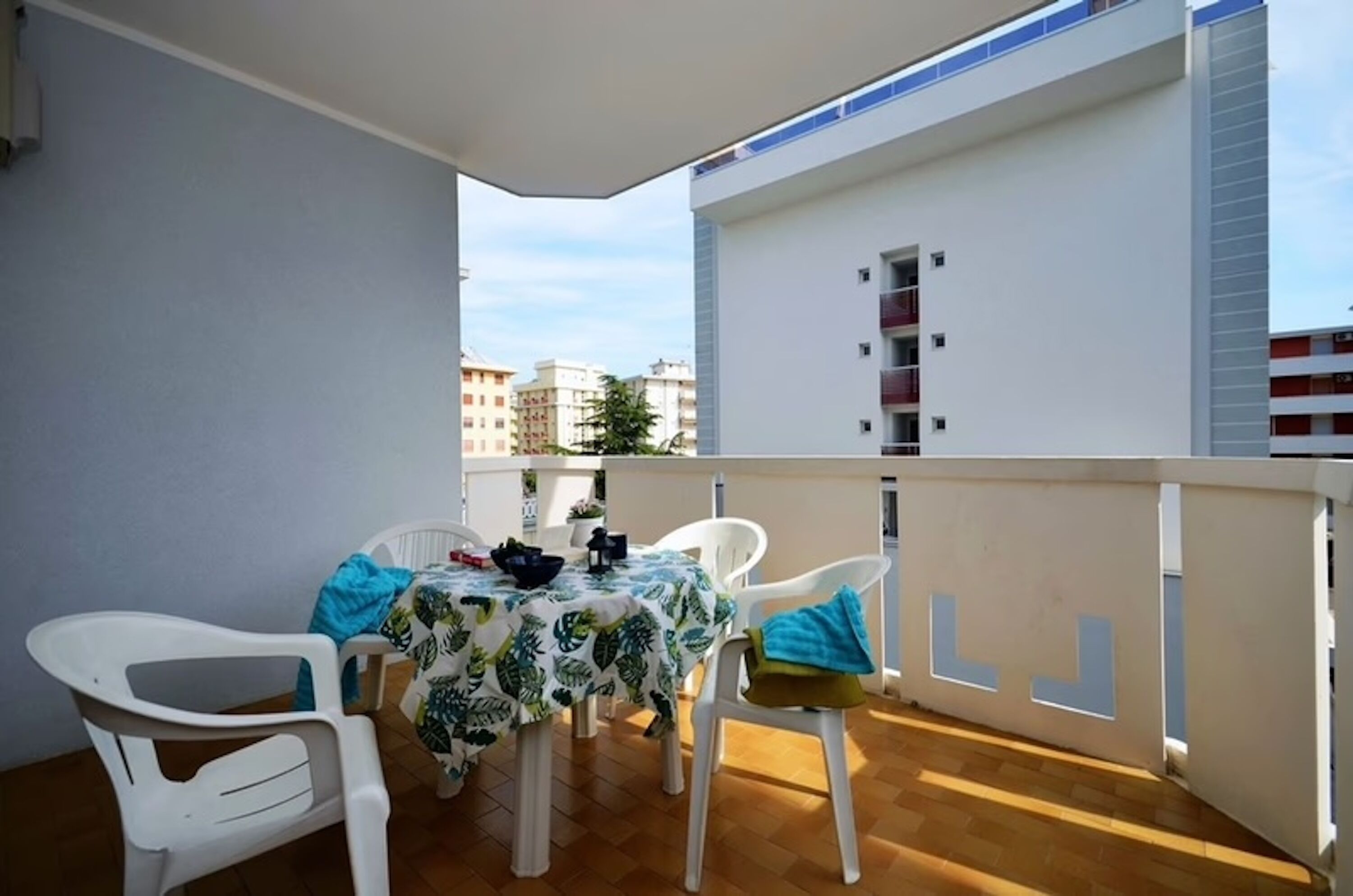 Ein Balkon mit Tisch und Stühlen, Blick auf Gebäude und einem weißen Geländer.