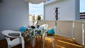 Ein Balkon mit Tisch und Stühlen, Blick auf Gebäude und einem weißen Geländer.