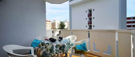 A balcony with a table and chairs, a view of buildings, and a white railing.