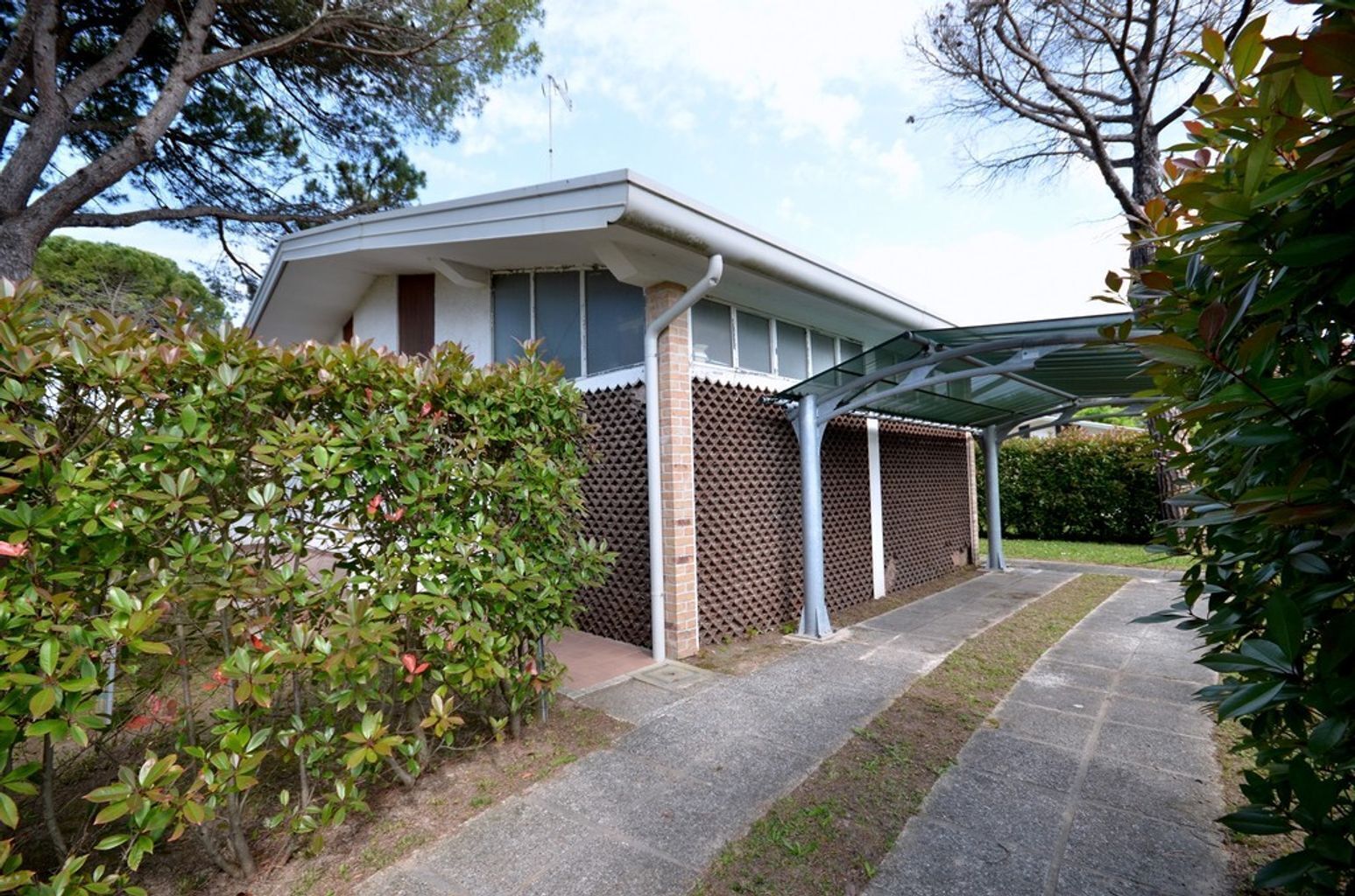 A modern house with a covered porch, a brick wall with a diamond pattern, and a paved driveway.