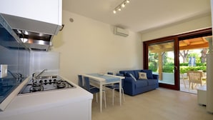 A compact kitchen with a gas stove, a dining table with chairs, a blue sofa, and a sliding glass door leading to an outdoor area.