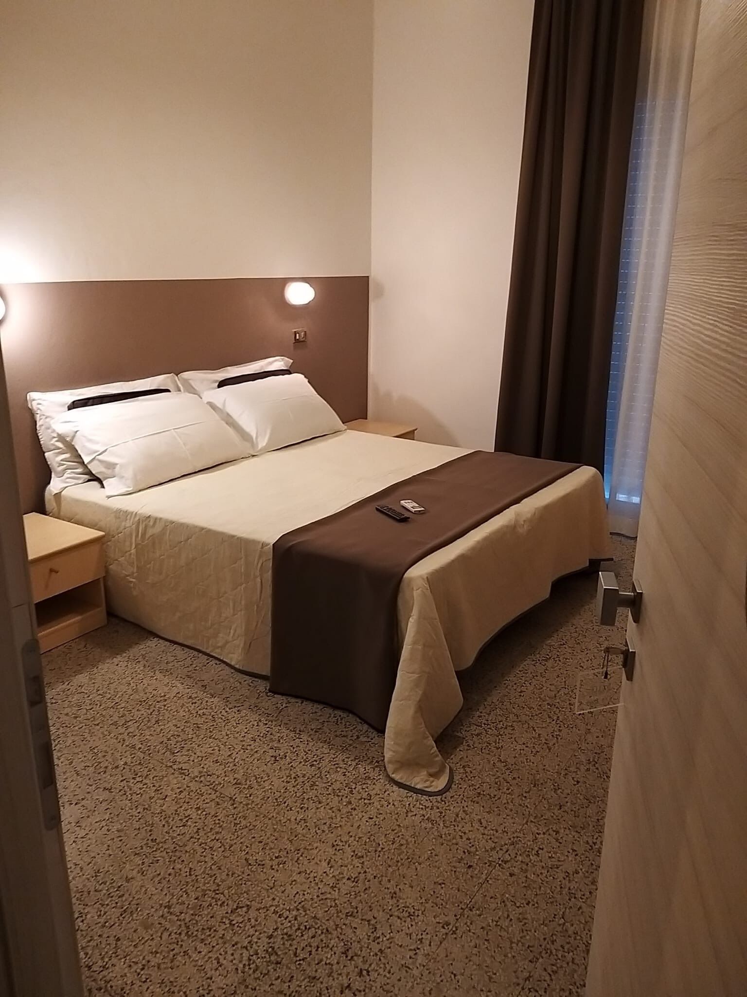 A neatly made bed with a brown headboard, a bedside table, and a remote control on the bed.