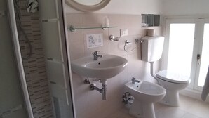A bathroom with a sink, two toilets, a shower, and a mirror. - Hotel Ideal  (Rimini)